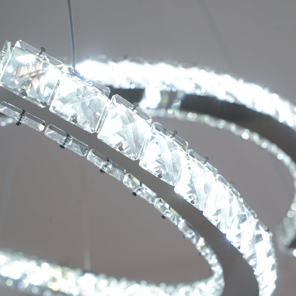 Close view of the lit crystals along one crescent of this Clérachic pendant, glowing white against a grey ceiling.