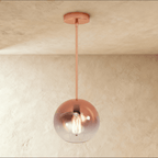 Clérachic rose gold glass sphere pendant catches warm light against a soft plaster ceiling and wall backdrop.