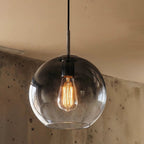 Clérachic pendant close-up shows the clear glass sphere shade and exposed Edison filament bulb glowing inside.