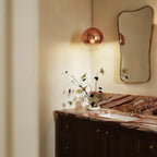 Clérachic rose gold glass sphere pendant hangs beside a bathroom vanity mirror above a veined stone counter.