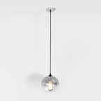 Clérachic silver-finish pendant light drops from a chrome ceiling canopy, glass sphere glowing softly white.