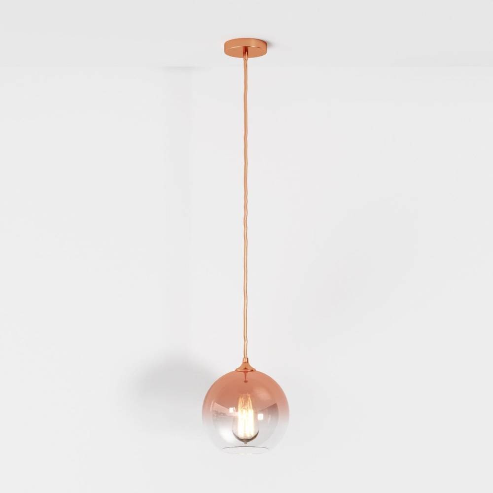 Clérachic rose gold pendant light drops from a matching ceiling canopy, glass sphere glowing softly on white.