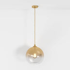 Clérachic champagne-finish pendant light hangs from a slim brass cord, sphere shade glowing on white backdrop.