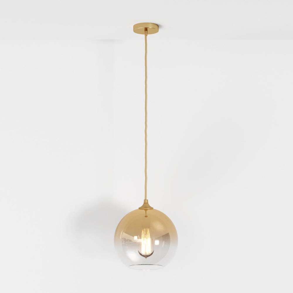 Clérachic champagne pendant light with gradient glass sphere shade, filament bulb glowing on a white backdrop.