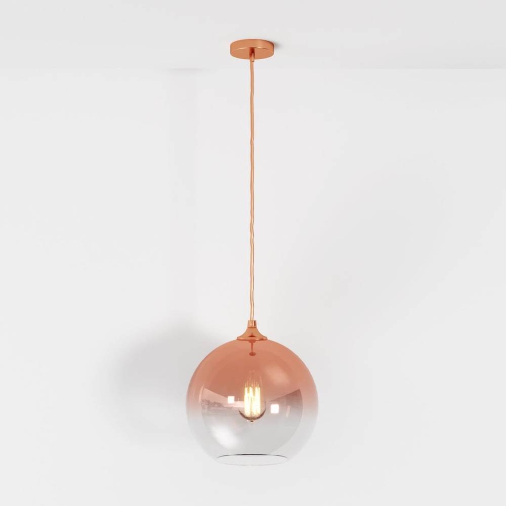 Clérachic rose gold pendant light with gradient glass sphere shade, filament bulb glowing on a white backdrop.