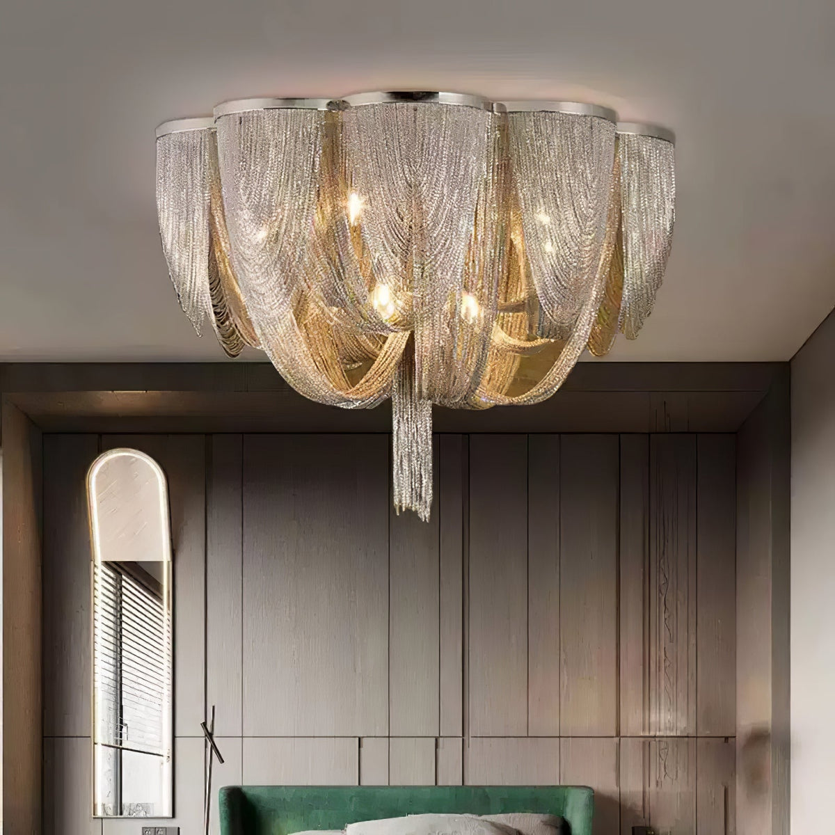 Lit Clérachic silver chain ceiling light above a dark panelled wall, an arched mirror and the edge of a green bed.