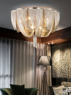 Clérachic chain ceiling light lit above grey curtains, a stone-textured wall and a tripod floor lamp.