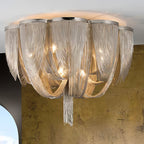 Close view of the layered silver chain swags and warm bulbs inside this Clérachic ceiling light, against a bronze wall.