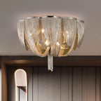 Clérachic silver chain ceiling light with a long centre tassel, hung in front of a dark panelled wall and an arched mirror.