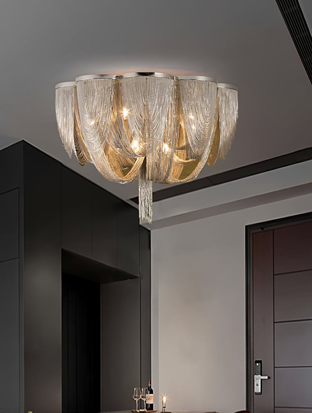 Smaller view of a Clérachic chain ceiling light in a dark-walled room beside a dark door and a table with glasses.