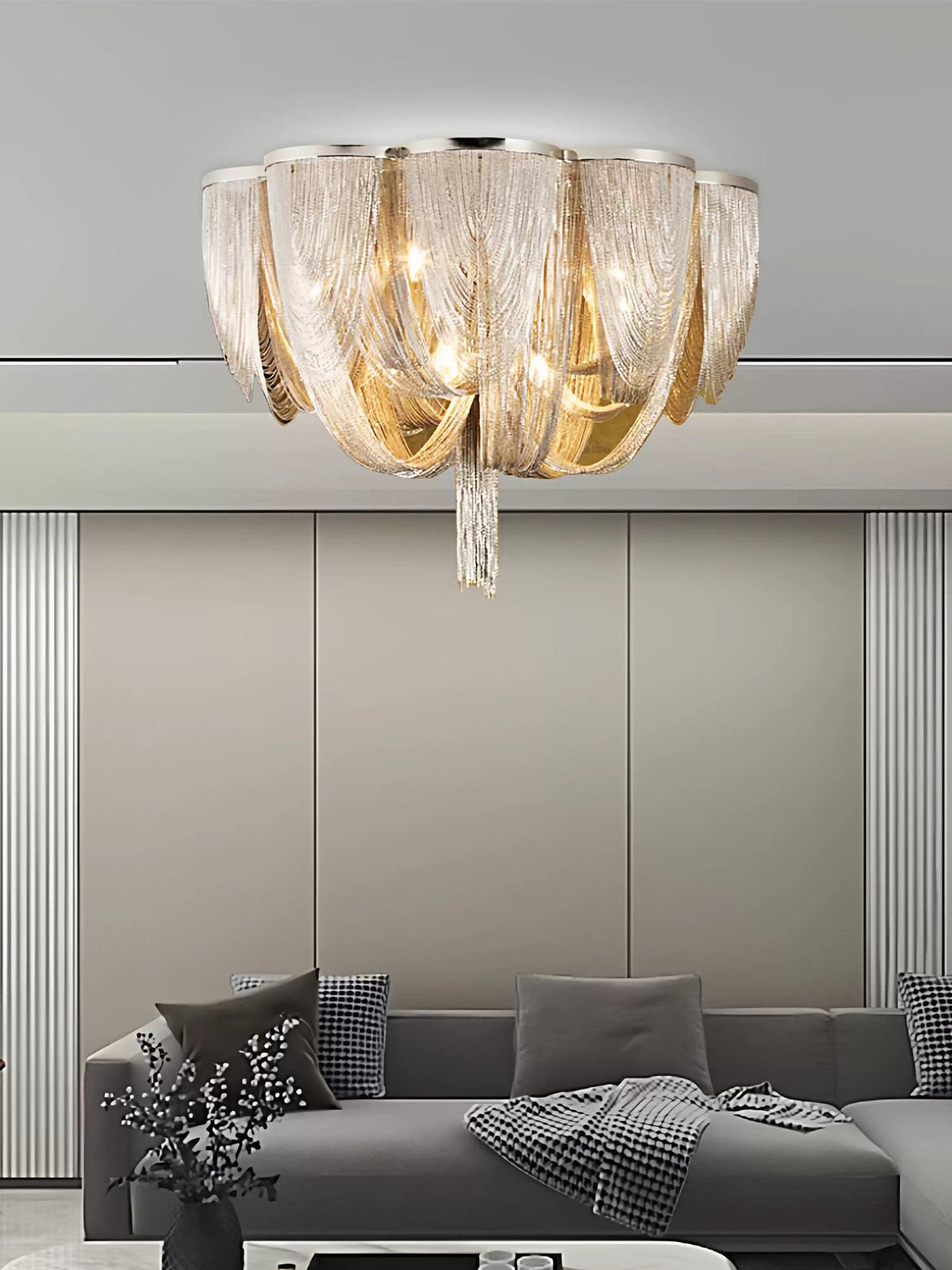 Clérachic silver chain ceiling light above a grey sofa with a throw, against a pale wall with vertical panels.