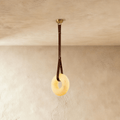 Clérachic alabaster ring pendant light glowing warm, hung from a brown leather strap and gold canopy on a limewash wall.