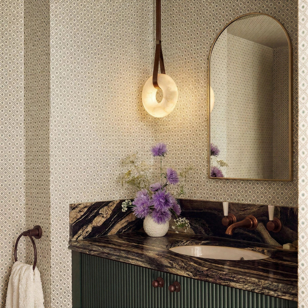 Clérachic alabaster ring pendant light glowing beside an arched mirror above a green vanity and patterned wallpaper.