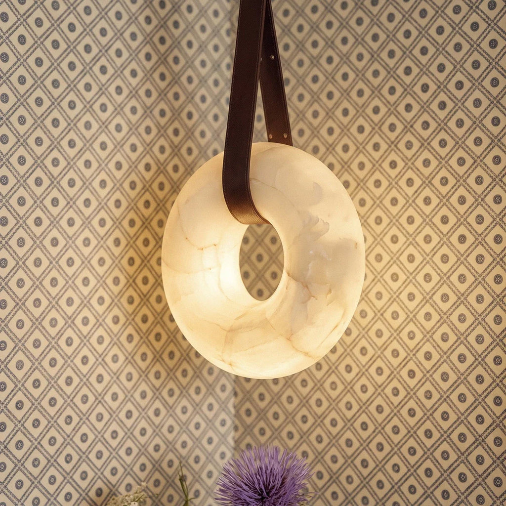 Close view of the Clérachic alabaster ring pendant light, its veined stone glowing softly against geometric wallpaper.
