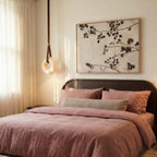 Clérachic alabaster ring pendant light hung low beside a bed with dusty pink linen and a dark wood headboard.