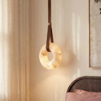 Clérachic alabaster ring pendant light close to a bedside curtain, its stone glowing warmly with veined detail.