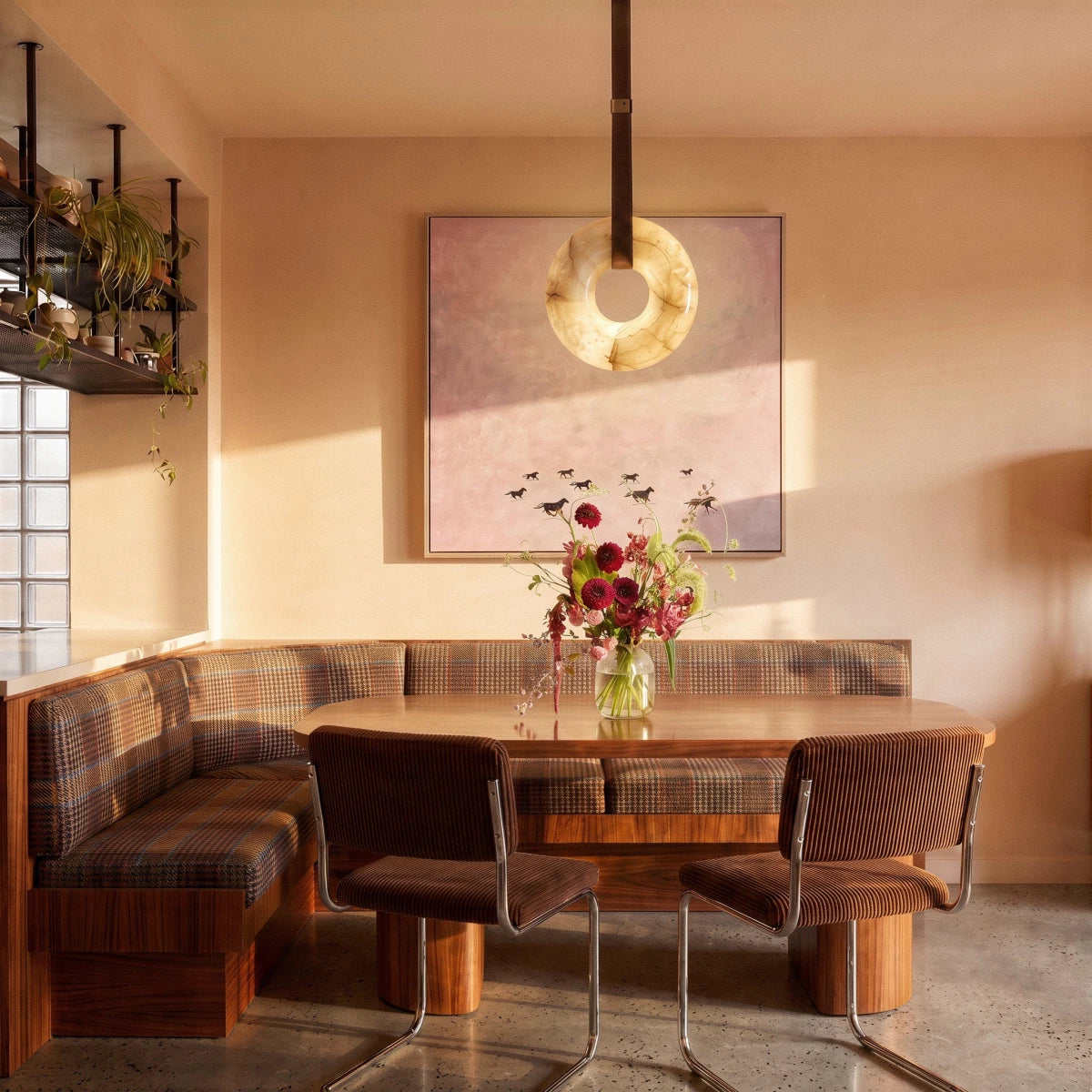 Clérachic alabaster ring pendant light hung on a leather strap above a corner dining nook with a wooden table.