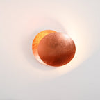 Small copper-toned Clérachic wall light on a blush-grey wall, two discs overlapping with a soft light around the edges.