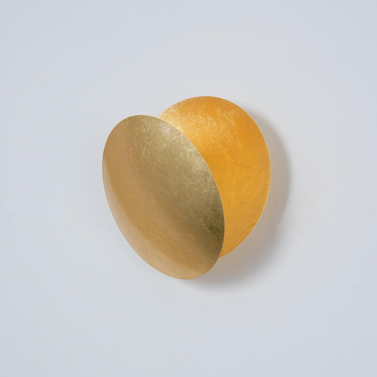 Unlit Clérachic wall light in gold, its front disc angled forward to reveal a deeper amber disc behind, on a pale grey wall.