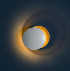 Clérachic wall light on a deep navy wall, a pale disc in front of a gold one, with a warm halo of light around the pair.