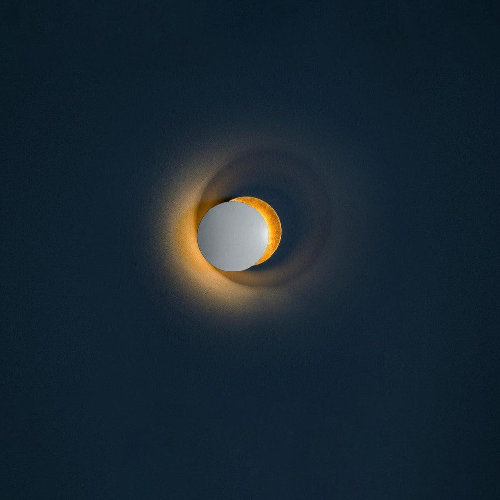 Small Clérachic wall light on a dark navy wall, a pale disc beside a gold one, with a faint amber light along the rim.
