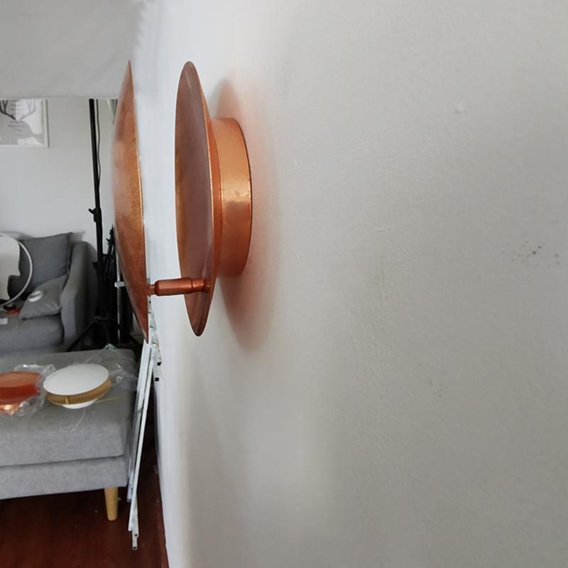 Side view of this Clérachic wall light fixed to a white wall, a copper disc standing off a round backplate in a living room.