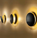 Three Clérachic wall lights in a row on a warm wall, each with a black disc and a gold disc glowing behind it.