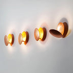 Four Clérachic wall lights in a line along a white wall, copper discs set at different angles with a golden glow inside each.