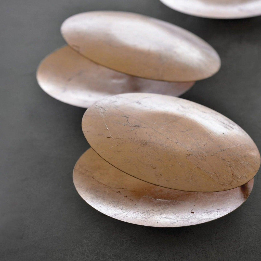 Close view of the crackled, pale rose-gold leaf finish on overlapping discs of this Clérachic wall light, laid on a dark grey surface.