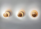 Three Clérachic wall lights in a row on a pale wall, each in a different gold or bronze tone, all lit with a soft glow.