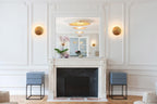Two small Clérachic wall lights flanking a mirror above a white marble fireplace in a panelled room with grey bedside tables.