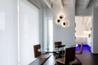 Three dark-finished Clérachic wall lights grouped on a white column in an open-plan dining room with a glass table.