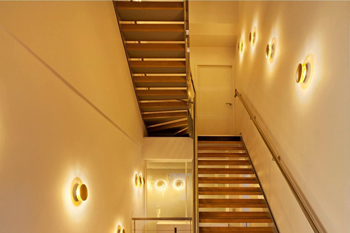 Looking down a staircase with Clérachic wall lights at intervals along the wall, each giving off a gentle golden light.