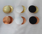 Six sample finishes of this Clérachic wall light laid out on white paper: gold, white and black fronts, each over a gold or copper disc.
