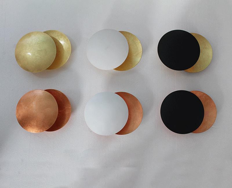 Six sample finishes of this Clérachic wall light laid out on white paper: gold, white and black fronts, each over a gold or copper disc.