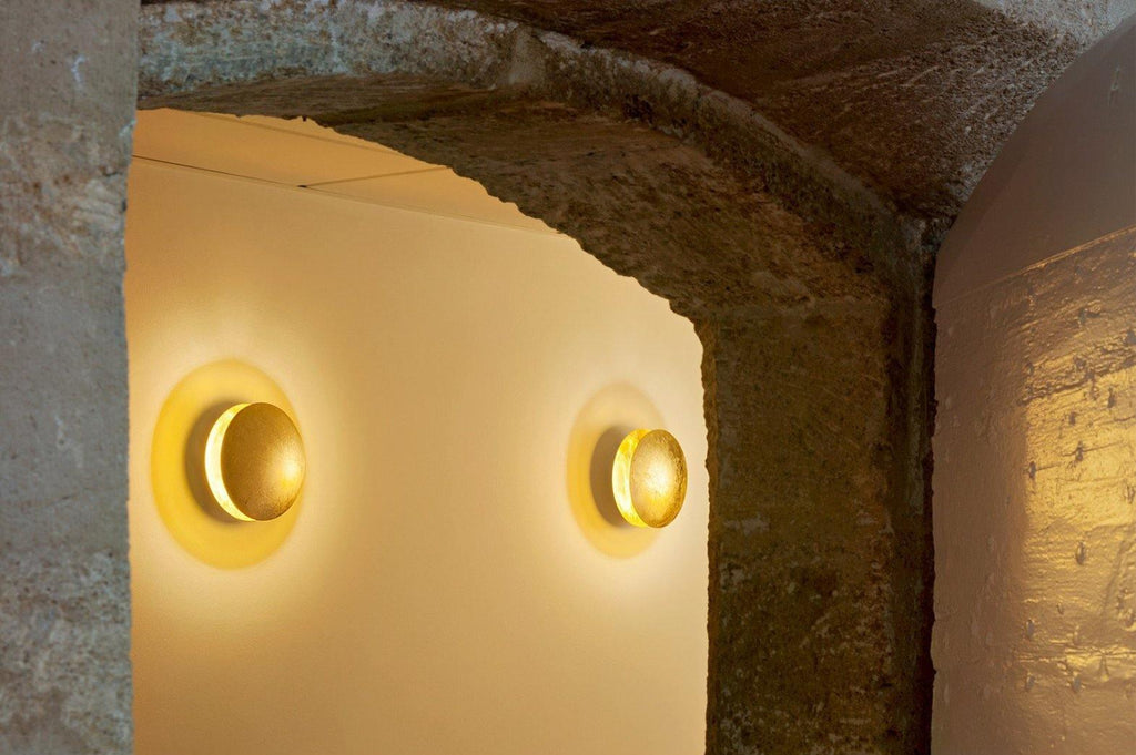 Two Clérachic wall lights glowing gold inside a rough stone arch, shown in a slightly tighter crop of the same scene.