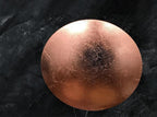 Rose-copper disc of this Clérachic wall light seen head-on against a dark, textured slate-grey wall, with a crackled leaf finish.