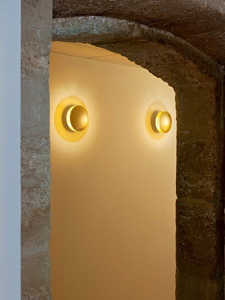 Two gold Clérachic wall lights glowing in a stone archway, seen in a tall crop with the rough masonry framing the light.