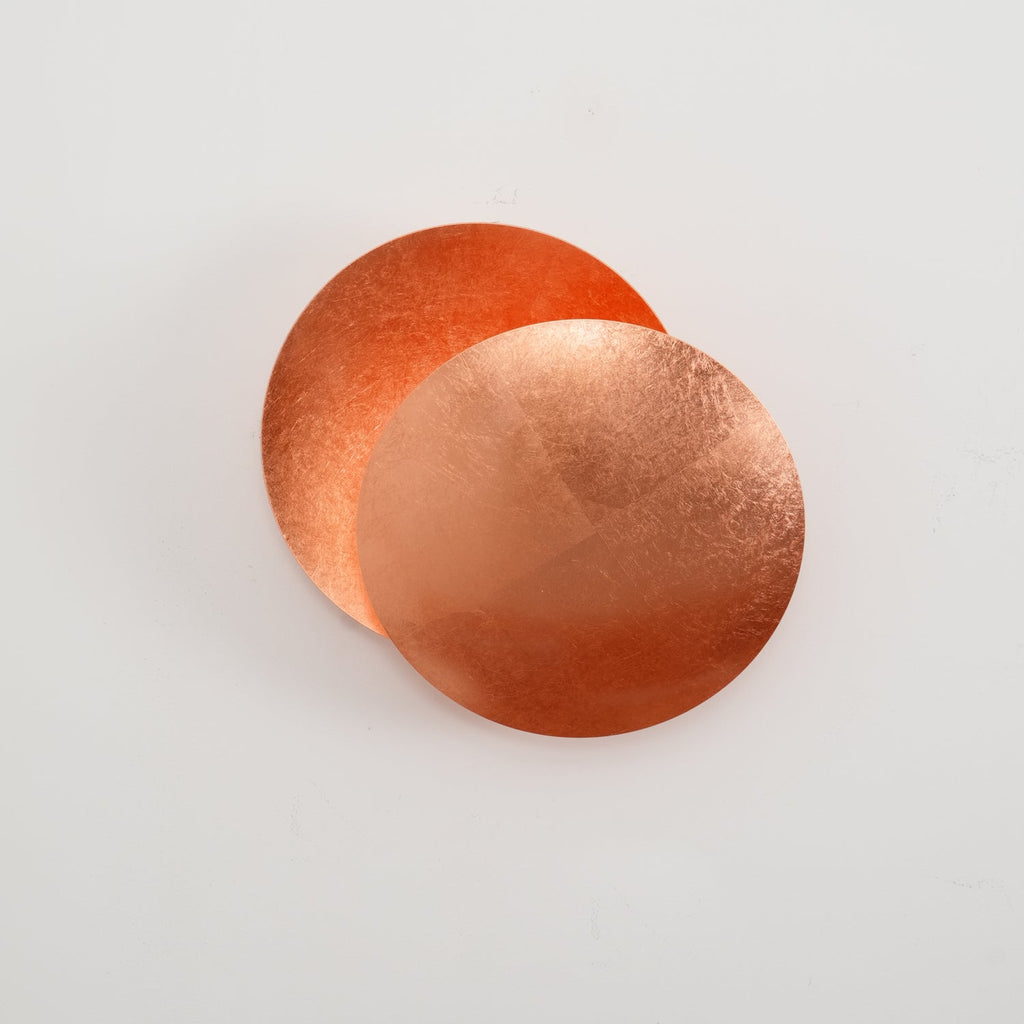 Copper Clérachic wall light on a pale wall, two overlapping discs with the rear disc cupped and glowing orange inside.