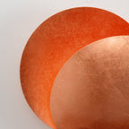Close view of the two overlapping copper-leaf discs on this Clérachic wall light, the rear disc glowing a richer orange.