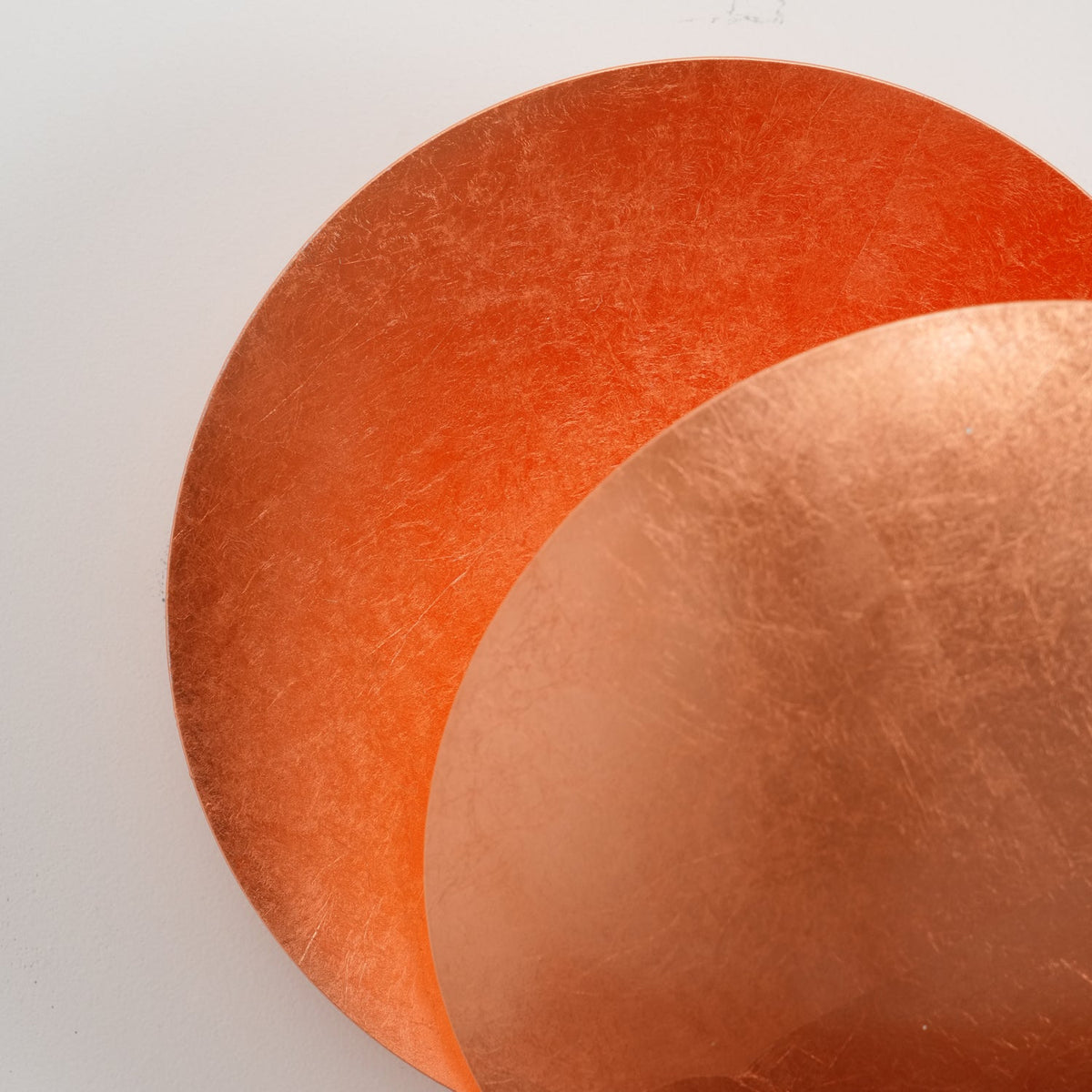 Close view of the two overlapping copper-leaf discs on this Clérachic wall light, the rear disc glowing a richer orange.