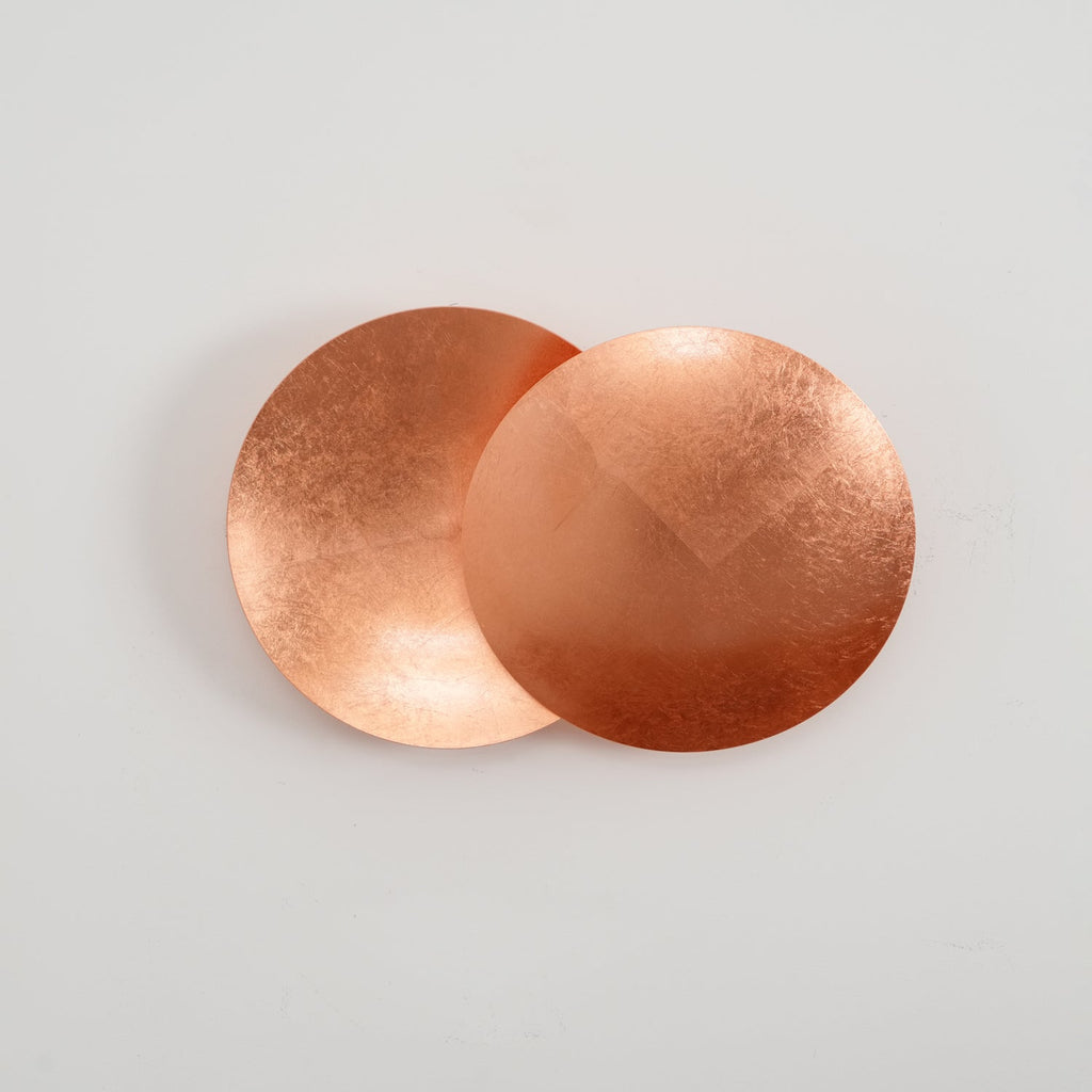 Straight-on view of this copper Clérachic wall light on a white wall, the rear disc curved like a shallow dish behind the flat front disc.