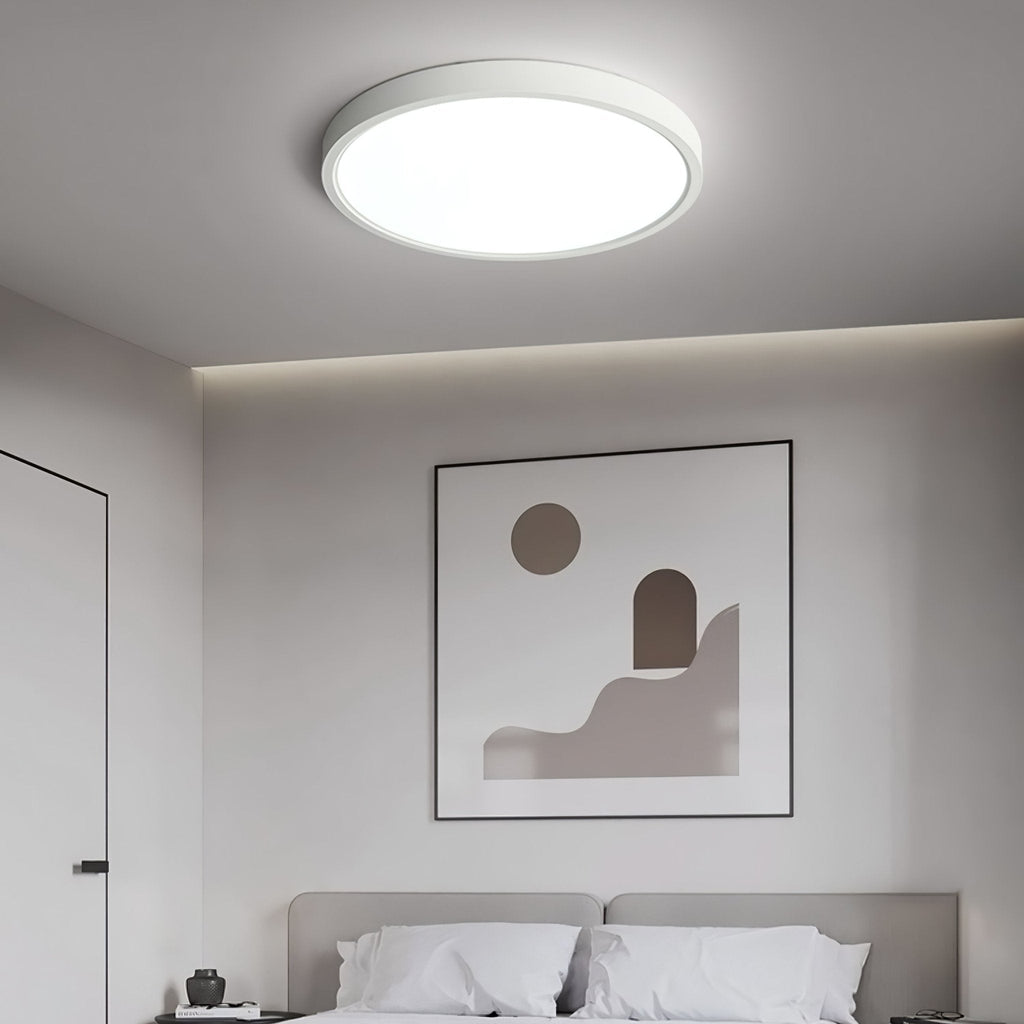 A white Clérachic round ceiling light glows above a grey bedroom with a framed abstract print and a bed with white pillows.