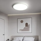 A white Clérachic round ceiling light glows above a grey bedroom with a framed abstract print and a bed with white pillows.