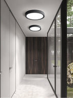 Two black Clérachic round ceiling lights, one large and one small, run down a pale corridor with a glass wall and a dark wood door.
