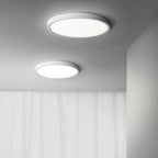 Two white Clérachic round ceiling lights of different sizes shine from a grey ceiling above a pale curtain.