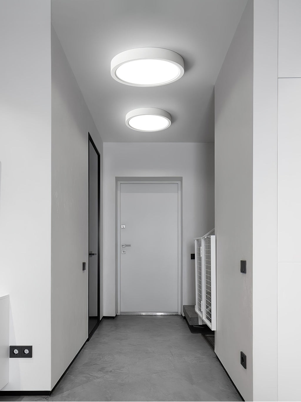 Two white Clérachic slim ceiling lights, one larger, light a narrow grey hallway with a white door at the far end.