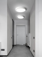 Two white Clérachic slim ceiling lights, one larger, light a narrow grey hallway with a white door at the far end.
