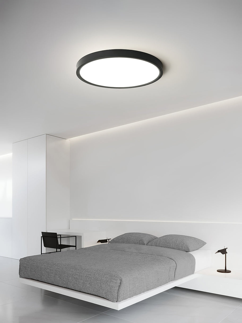 A black-rimmed Clérachic round ceiling light hangs above a minimal white bedroom with a low grey bed and a concealed cove light.