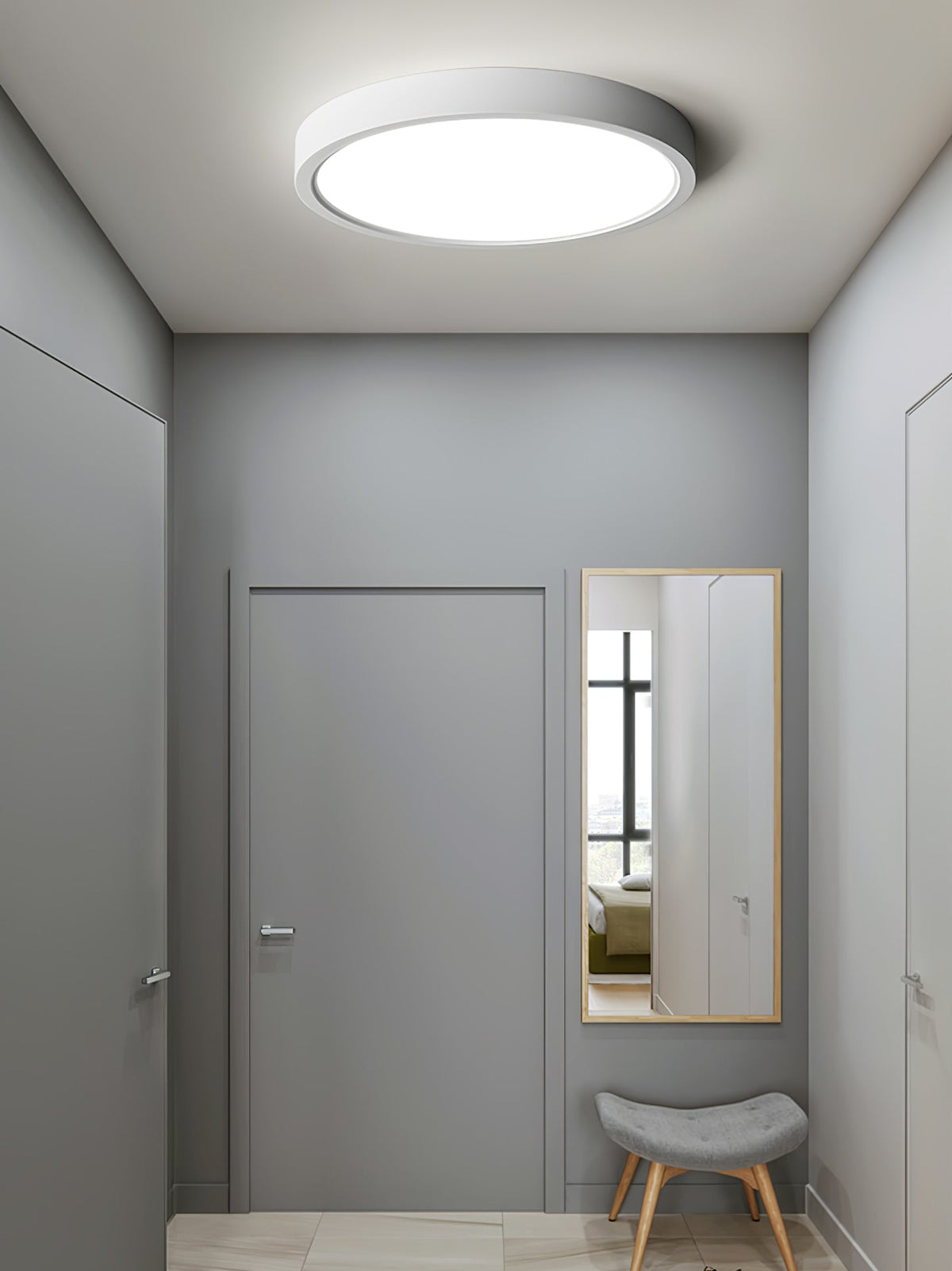 A small grey hallway with a closed door, a long mirror and a low stool, lit by a white Clérachic round ceiling light.
